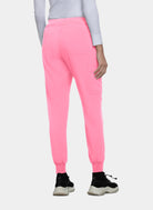 Women's bright pink jogger scrub trousers with ribbed cuffs, back patch pockets, and utility pocket, shown from the rear, worn by a model.
