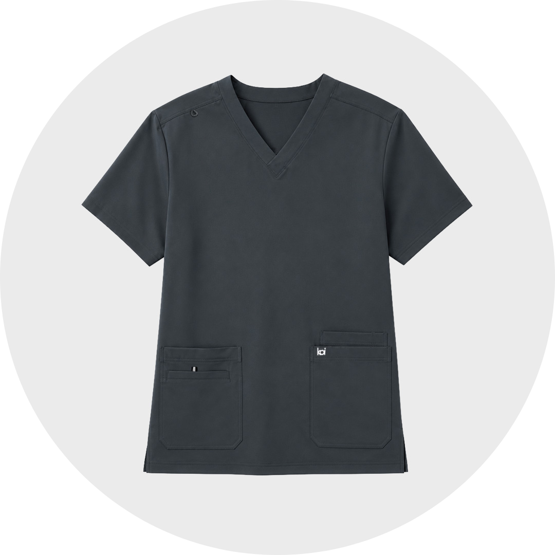 A dark gray V-neck scrub top with short sleeves and two front pockets, displayed on a light gray circular background.
